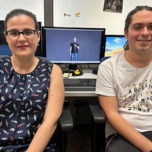 Two researchers are seated in front of monitors displaying a virtual avatar using sign language. The workspace reflects their development of a real-time sign language translation app.